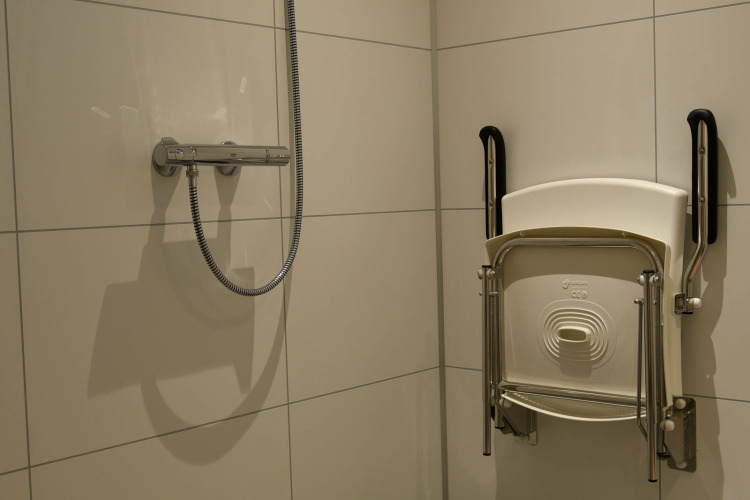 Duschbereich mit klappbarem Sitz und Haltegriffen an der Wand im River Lodge, Camping de Koeksebelt, Niederlande.