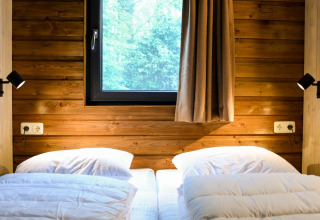 Dos camas individuales con ropa blanca junto a una ventana en River Lodge, Camping de Koeksebelt, Países Bajos.