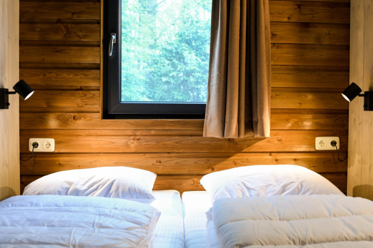 Dos camas individuales con ropa blanca junto a una ventana en River Lodge, Camping de Koeksebelt, Países Bajos.