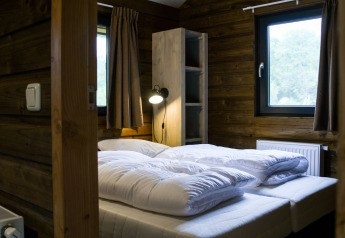 Cozy bedroom in River Lodge at Camping de Koeksebelt, Netherlands, featuring wood walls and bright windows.