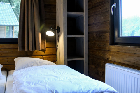 Dormitorio con paredes de madera, cama, lámpara y ventana en River Lodge de Camping de Koeksebelt, Países Bajos.