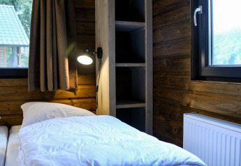 Dormitorio con paredes de madera, cama, lámpara y ventana en River Lodge de Camping de Koeksebelt, Países Bajos.