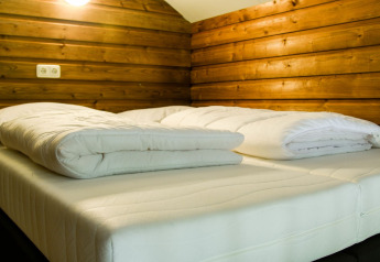 Letto accogliente con piumoni bianchi in una cabina di legno al River Lodge, Camping de Koeksebelt, Paesi Bassi.