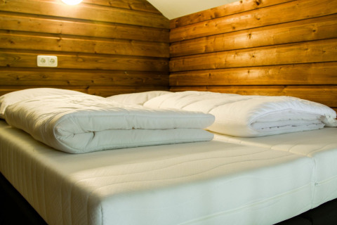 Cama acogedora con edredones blancos en una cabaña de madera del River Lodge, Camping de Koeksebelt, Países Bajos.