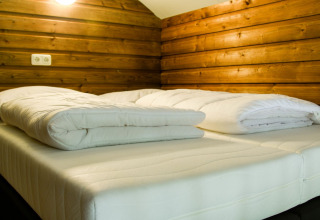 Cama acogedora con edredones blancos en una cabaña de madera del River Lodge, Camping de Koeksebelt, Países Bajos.