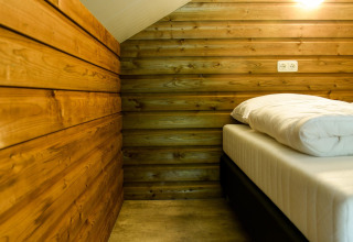 Indretning af soveområdet i River Lodge på Camping de Koeksebelt i Nederlandene med træpaneler og seng.