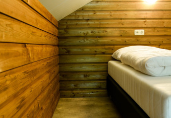 Slaapruimte in River Lodge op Camping de Koeksebelt in Nederland met houten wanden en comfortabel bed.