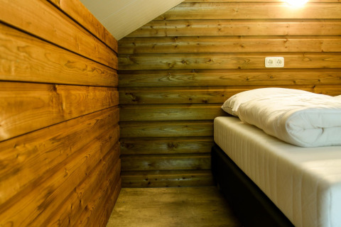 Indretning af soveområdet i River Lodge på Camping de Koeksebelt i Nederlandene med træpaneler og seng.