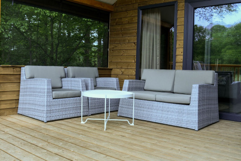 Udendørs loungeområde med grå kurvemøbler og bord på træterrasse ved River Lodge, Camping de Koeksebelt.
