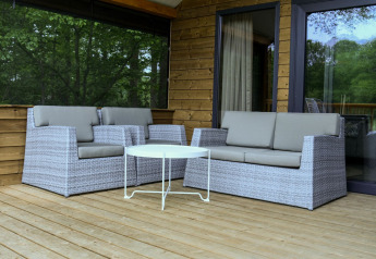 Zona exterior con sofás de mimbre gris y mesa en la terraza de madera del River Lodge, Camping de Koeksebelt.