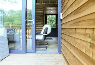 Porte ouverte sur la River Lodge au Camping de Koeksebelt, Pays-Bas, avec fauteuil moderne et murs en bois.