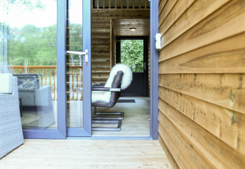 Porte ouverte sur la River Lodge au Camping de Koeksebelt, Pays-Bas, avec fauteuil moderne et murs en bois.