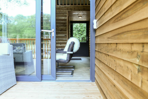 Puerta abierta hacia River Lodge en Camping de Koeksebelt, Países Bajos, con silla moderna y paredes de madera.