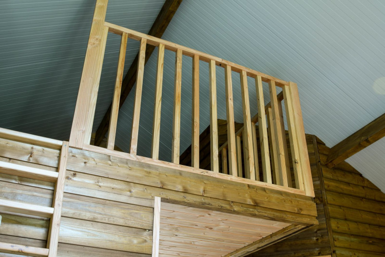 Innenansicht einer Holzhütte mit Zwischengeschoss und Geländer in der River Lodge, Camping de Koeksebelt.