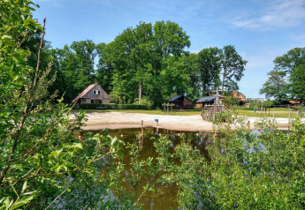 River Lodge aan Camping de Koeksebelt in Nederland met zandstrand, meer, huisjes en groene omgeving.