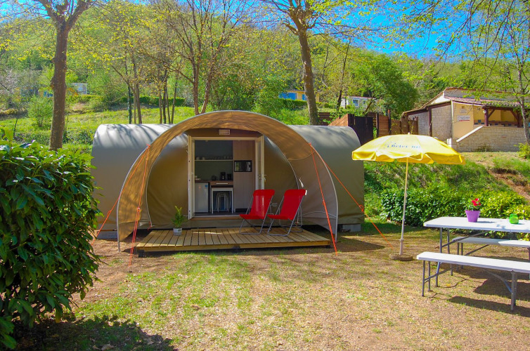 Tienda safari Le Petit Chateau en La Draille, Francia, con dos sillas rojas y mesa de picnic afuera.
