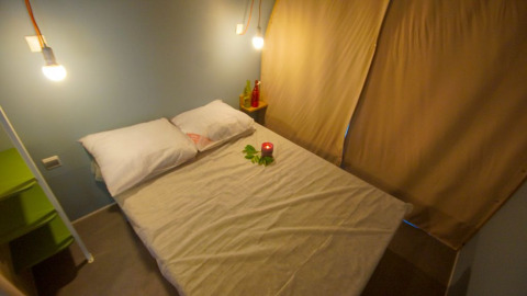 Slaapruimte in safaritent Le Petit Chateau bij La Draille in Frankrijk, met gezellig bed en warme verlichting.