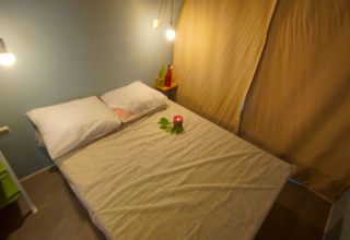 Slaapruimte in safaritent Le Petit Chateau bij La Draille in Frankrijk, met gezellig bed en warme verlichting.
