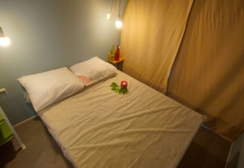 Slaapruimte in safaritent Le Petit Chateau bij La Draille in Frankrijk, met gezellig bed en warme verlichting.