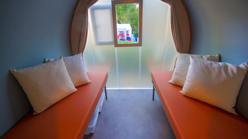 Vista interior de una tienda safari Le Petit Chateau con dos camas y cojines blancos en La Draille, Francia.