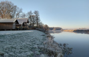 Césped cubierto de escarcha y cabañas de madera junto al río en River Cottage, Camping de Koeksebelt, Países Bajos.