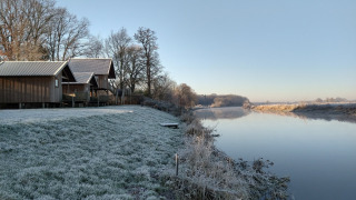 Césped cubierto de escarcha y cabañas de madera junto al río en River Cottage, Camping de Koeksebelt, Países Bajos.