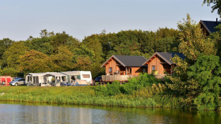 Vista sui lodge River Cottage e caravan vicino al lago a Camping de Koeksebelt, Paesi Bassi, immersi nella natura.