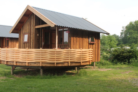 River Cottage au Camping de Koeksebelt, Pays-Bas, chalet en bois avec terrasse dans un cadre verdoyant.