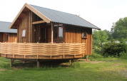 River Cottage au Camping de Koeksebelt, Pays-Bas, chalet en bois avec terrasse dans un cadre verdoyant.