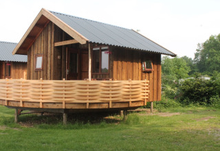 River Cottage au Camping de Koeksebelt, Pays-Bas, chalet en bois avec terrasse dans un cadre verdoyant.