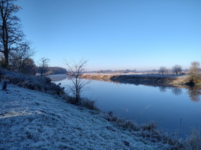 Hierba escarchada y río tranquilo en River Cottage, Camping de Koeksebelt, Países Bajos, en un día invernal claro.