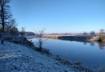 Hierba escarchada y río tranquilo en River Cottage, Camping de Koeksebelt, Países Bajos, en un día invernal claro.