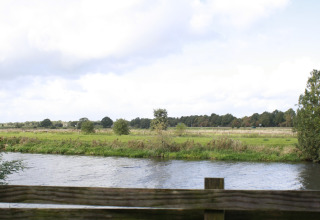 Vista desde River Cottage en Camping de Koeksebelt, Países Bajos, con río, campo y vegetación abundante.