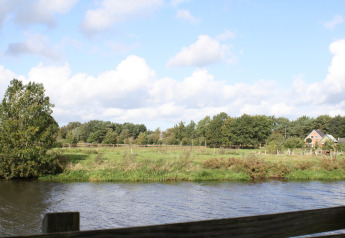 Vista su un fiume tranquillo, campi verdi e una casa al River Cottage, Camping de Koeksebelt, Paesi Bassi.