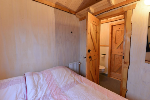 Chambre avec lit en bois et portes ouvertes vers la salle de bain à River Cottage, Camping de Koeksebelt, Pays-Bas.