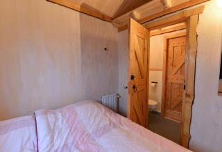 Chambre avec lit en bois et portes ouvertes vers la salle de bain à River Cottage, Camping de Koeksebelt, Pays-Bas.
