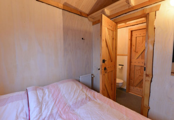 Dormitorio con cama de madera y puertas abiertas al baño en River Cottage de Camping de Koeksebelt, Países Bajos.