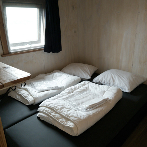 Deux lits simples avec couettes et oreillers blancs dans un chalet en bois à River Cottage, Camping de Koeksebelt.