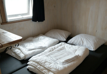 Twee enkele bedden met witte dekens en kussens in een houten hut bij River Cottage, Camping de Koeksebelt.