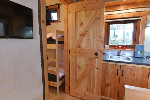 Vista interior de River Cottage en Camping de Koeksebelt, con cocina, literas y televisor en la pared.