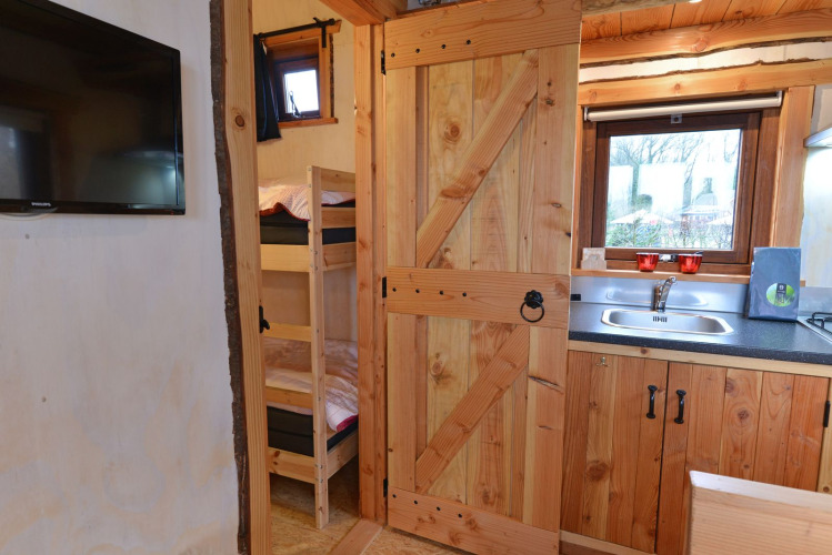 Vista interior de River Cottage en Camping de Koeksebelt, con cocina, literas y televisor en la pared.