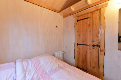 Chambre à River Cottage au Camping de Koeksebelt, Pays-Bas, avec porte en bois et lit douillet.
