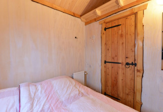 Dormitorio en River Cottage en Camping de Koeksebelt, Países Bajos, con puerta de madera y cama.