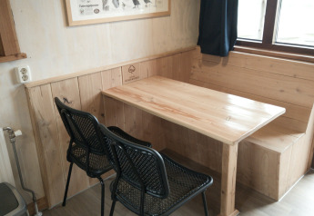 Eethoek met houten tafel, bank, twee zwarte stoelen en vogelposter in River Cottage, Camping de Koeksebelt.