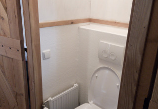 Un pequeño baño con inodoro blanco y puerta de madera en River Cottage, Camping de Koeksebelt, Países Bajos.