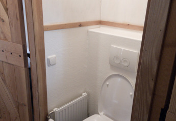 Piccola toilette con wc bianco e porta in legno a River Cottage, Camping de Koeksebelt, Paesi Bassi.