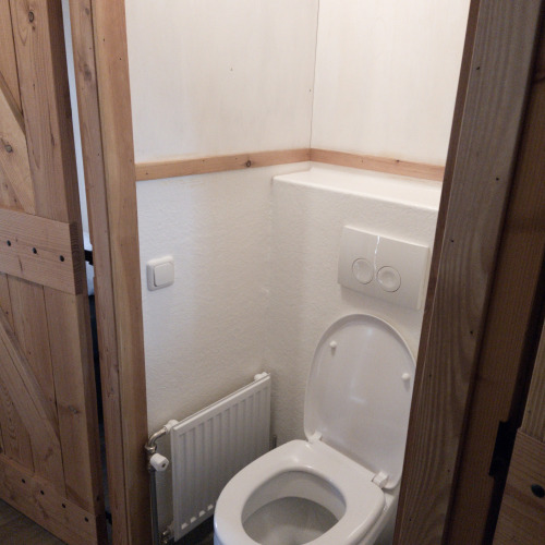 Un pequeño baño con inodoro blanco y puerta de madera en River Cottage, Camping de Koeksebelt, Países Bajos.