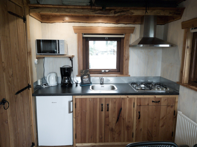 Cocina compacta en River Cottage de Camping de Koeksebelt, con gabinetes de madera y electrodomésticos.