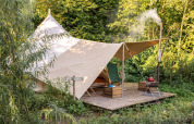 Una acogedora tienda tipi con lona y zona de descanso, situada sobre plataforma entre vegetación y bosque.