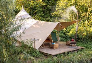 Una acogedora tienda tipi con lona y zona de descanso, situada sobre plataforma entre vegetación y bosque.